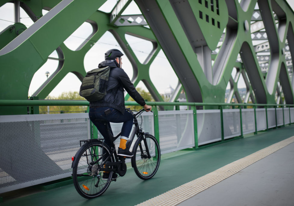 Rear view of a businessman commuter on the way to work, riding bike over bridge, sustainable lifestyle concept.