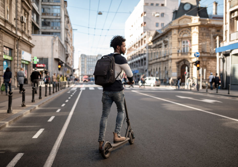Back view of a young African american man exploring the city using a scooter