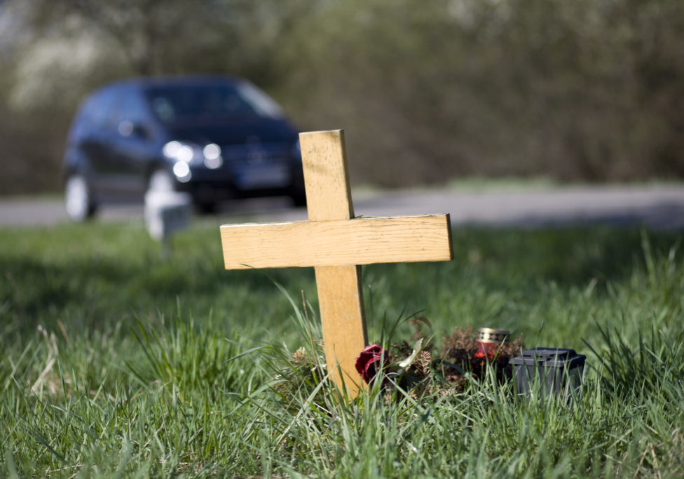 A wooden roadside memorial. In the background an unrecognisable car drives by the scenery. Selective focus